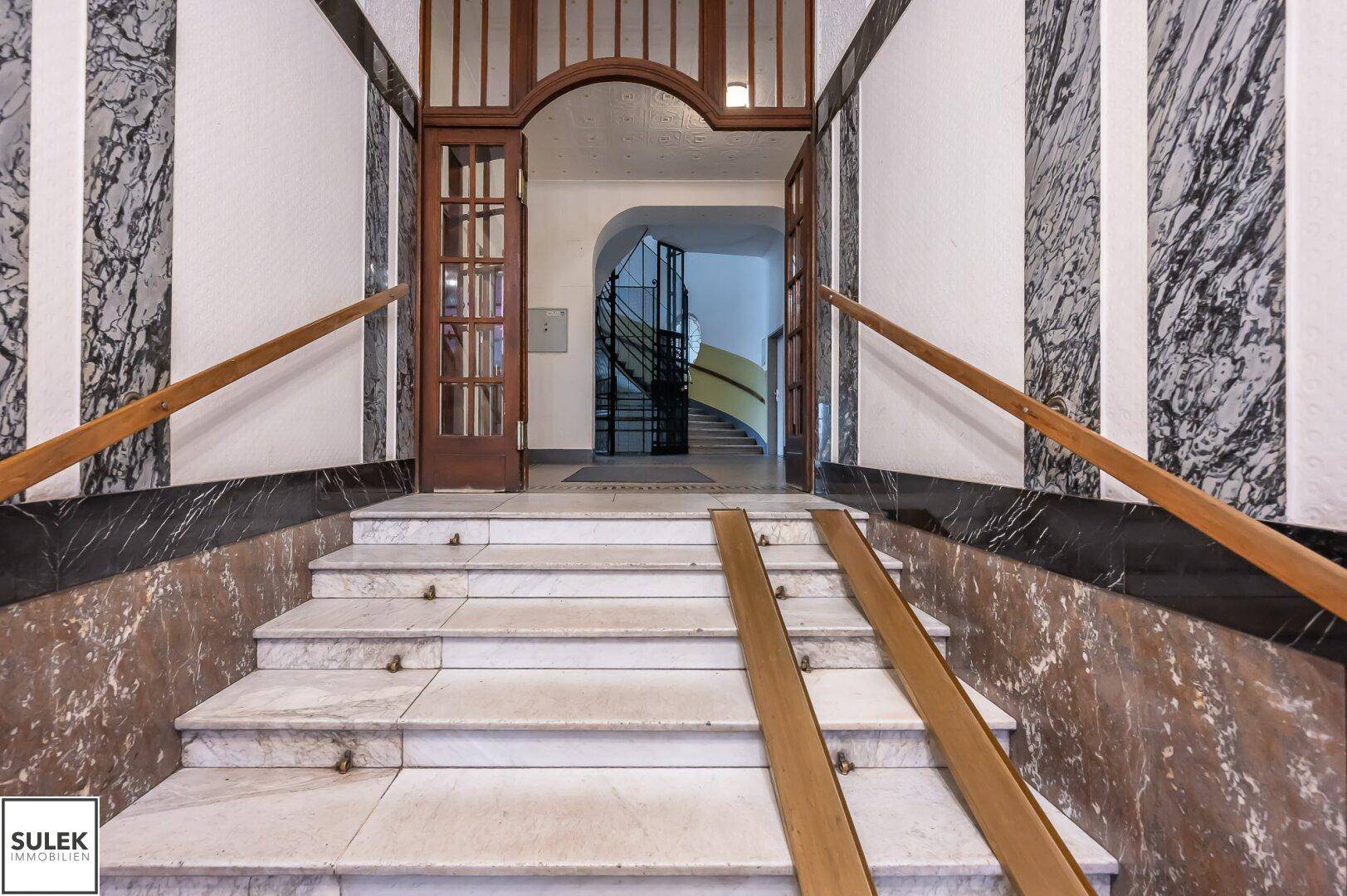 Historischer Eingangsbereich mit Marmortreppe, Holzgeländer und einer provisorischen Rampe für Barrierefreiheit.