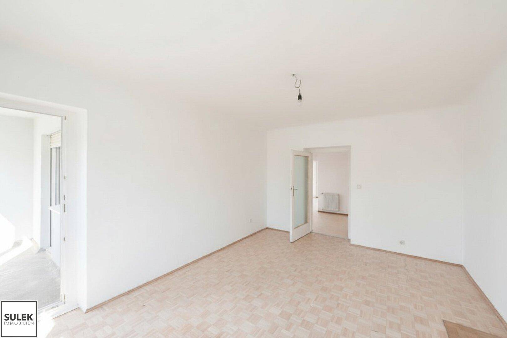 Geräumiges, unmöbliertes Zimmer mit Parkettboden und Zugang zu einem Balkon.