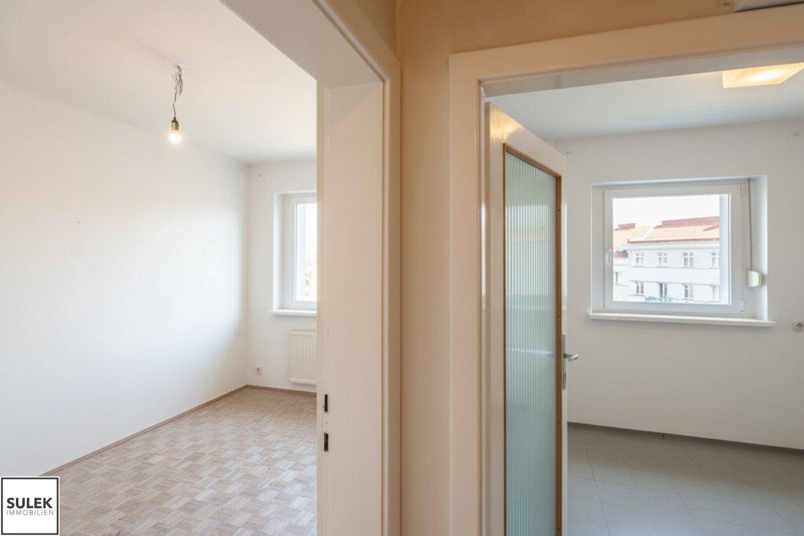 Blick durch eine Tür in ein weiteres Zimmer mit unterschiedlichen Bodenbelägen.