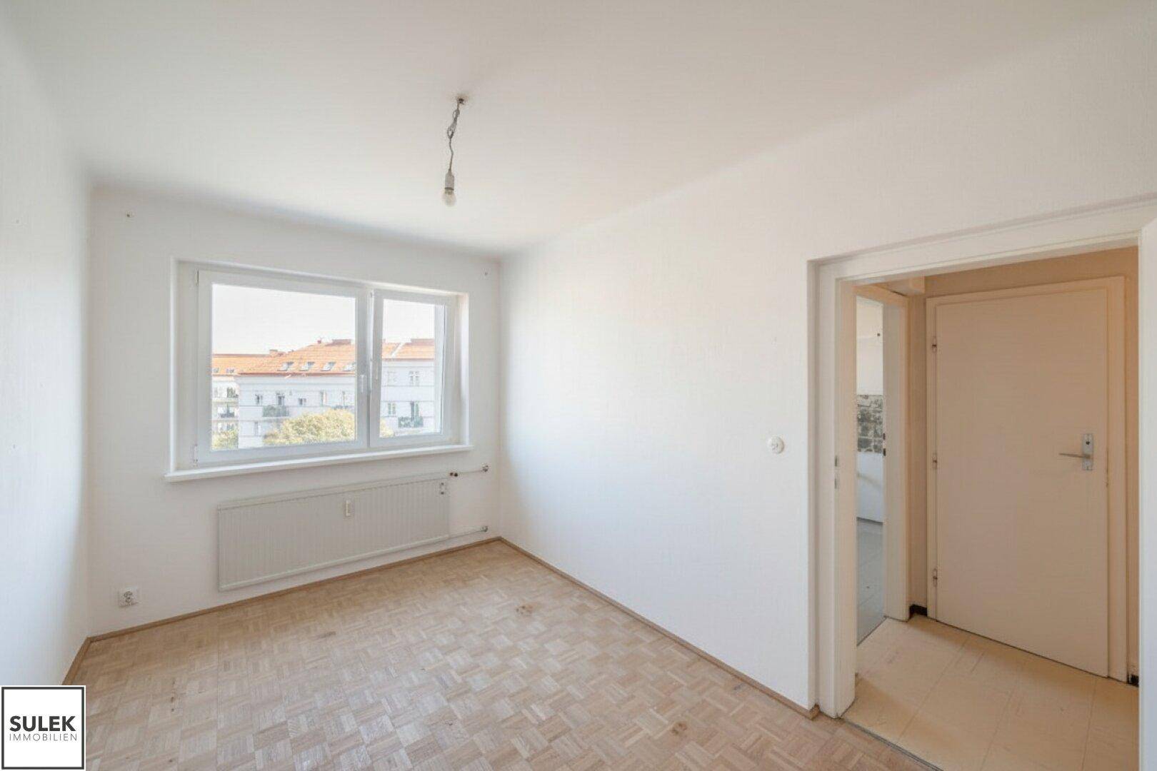 Helles, unmöbliertes Zimmer mit Parkettboden und Blick auf die umliegenden Gebäude.