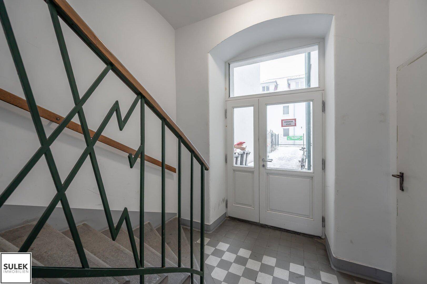 Treppenabsatz mit Steinstufen und einem Eingangsbereich mit schwarz-weiß kariertem Fliesenboden.