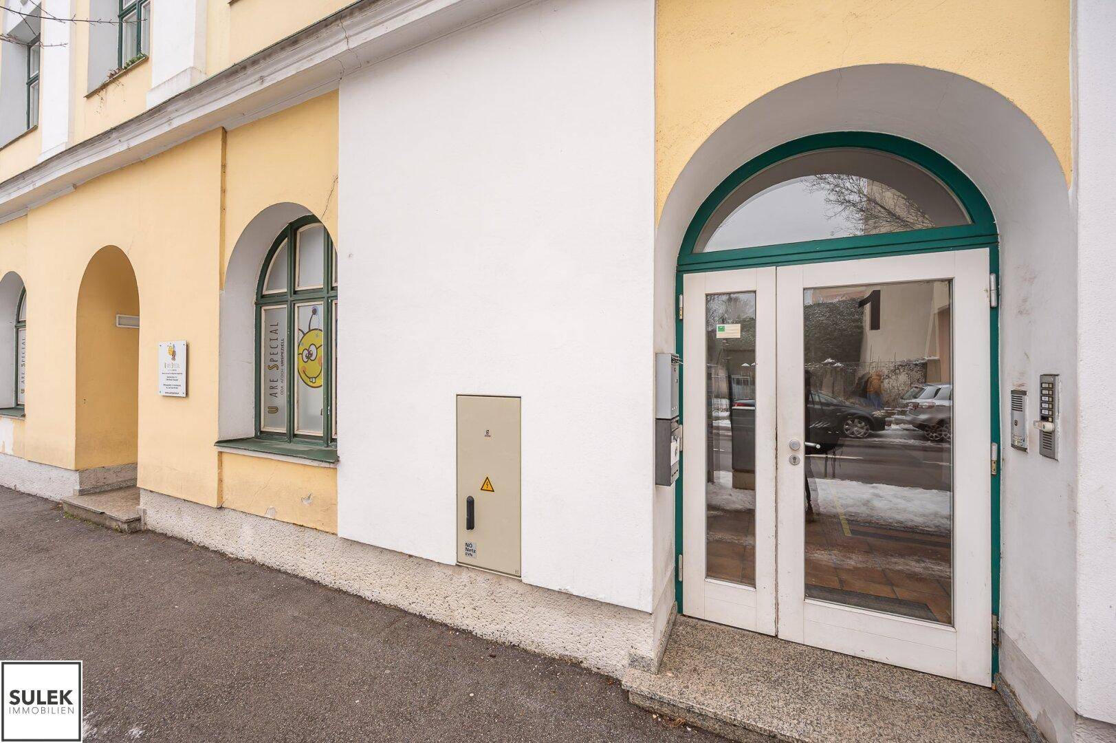 Eingangsbereich Nummer 1 mit grünen Türrahmen und einem Fenster mit Bienenmotiv.