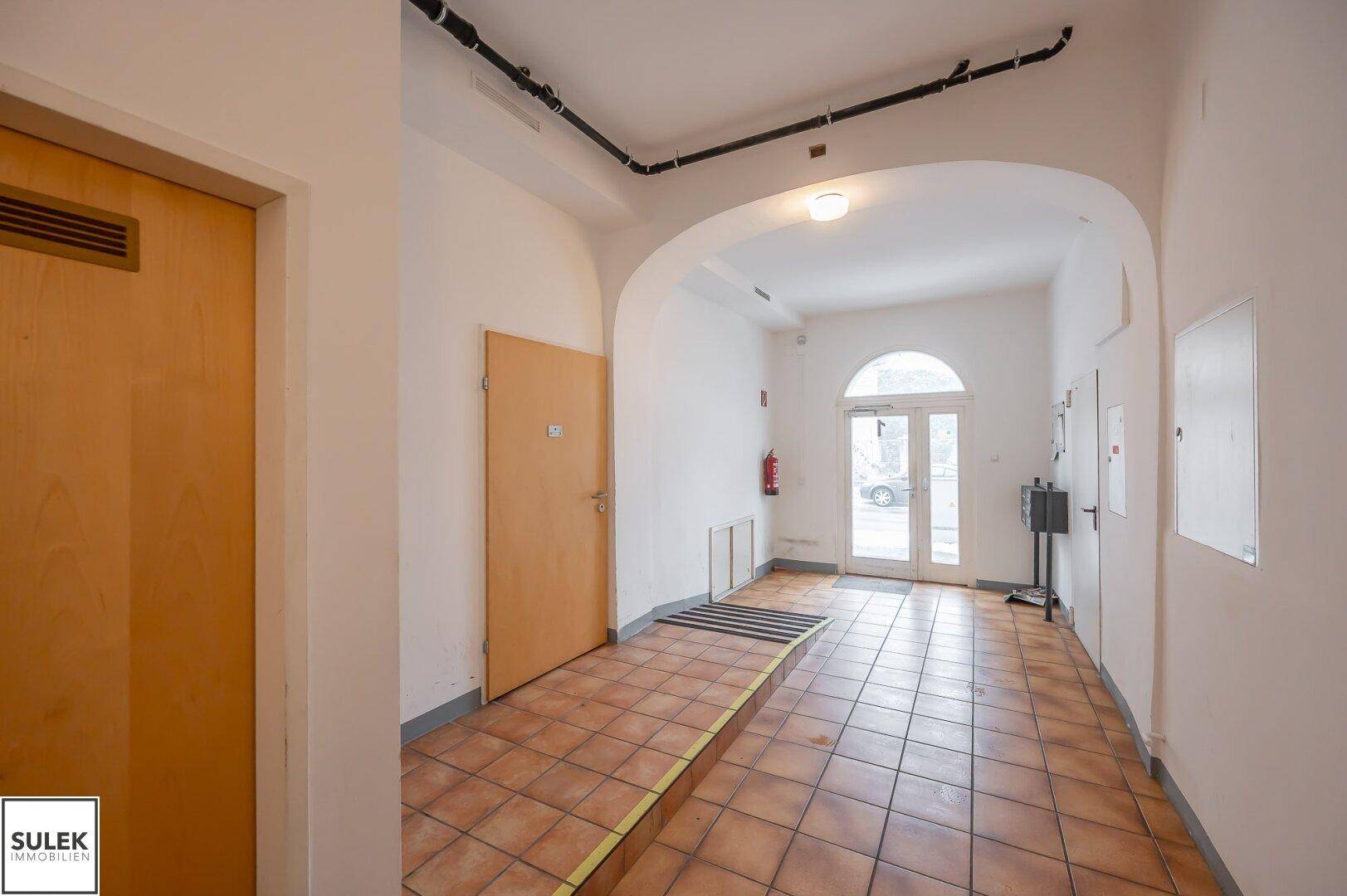 Geräumiger Flur mit Terrakotta-Fliesenboden und einem hellen Eingangsbereich mit Glastüren.