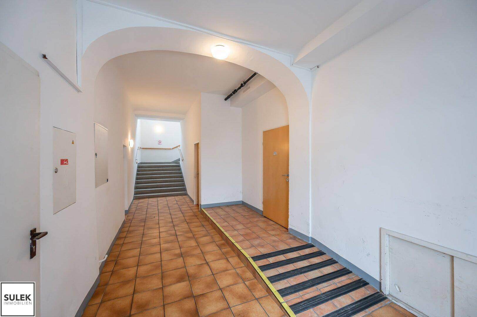 Eingangsbereich mit Fliesenboden und einer Rampe für barrierefreien Zugang zum Treppenhaus.