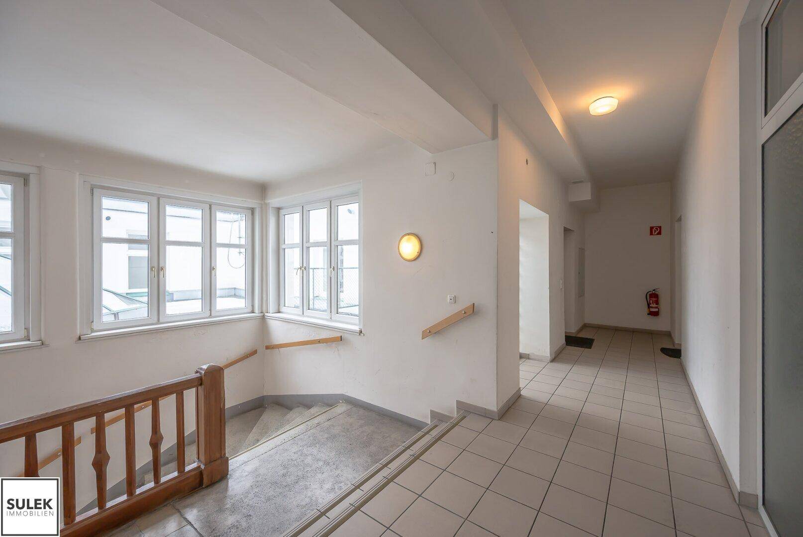 Treppenhaus mit Steinstufen und einem hellen Flur mit Fenstern, die den Raum erhellen.