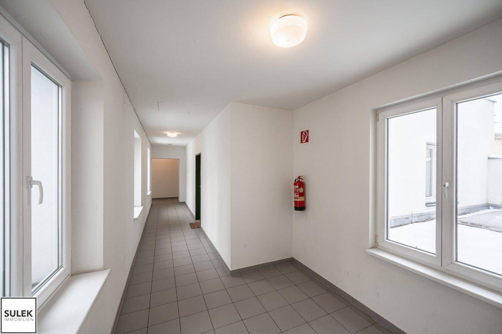 Langer, heller Flur mit Fliesenboden und mehreren Fenstern, die Tageslicht spenden.