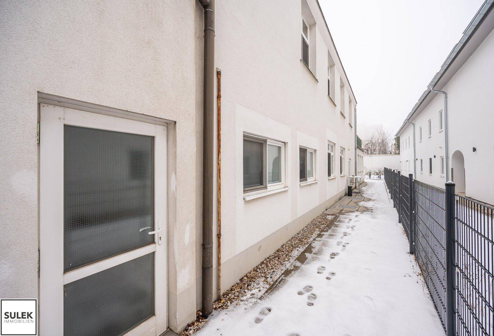 Seitenansicht des Gebäudes mit einem verschneiten Weg und einem Zaun.