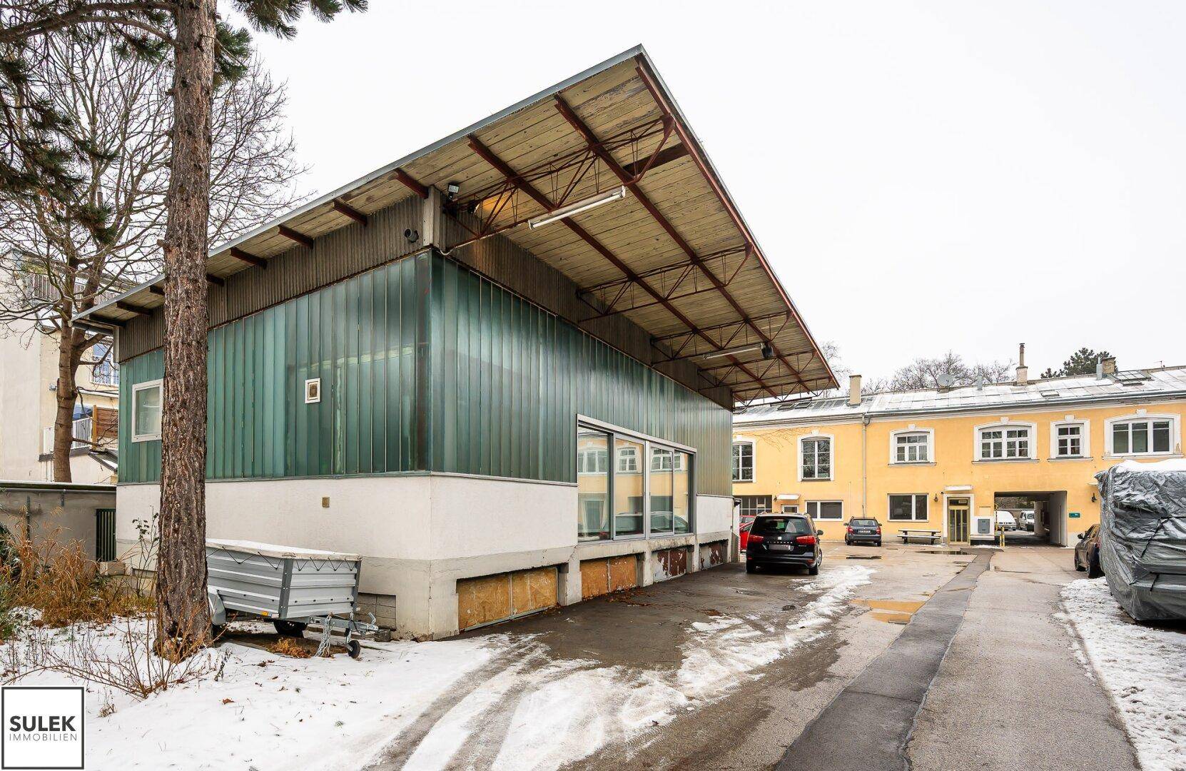 Außenansicht des Gebäudes mit markantem Dach und Glasfassade, umgeben von Bäumen und Schnee auf dem Gelände.