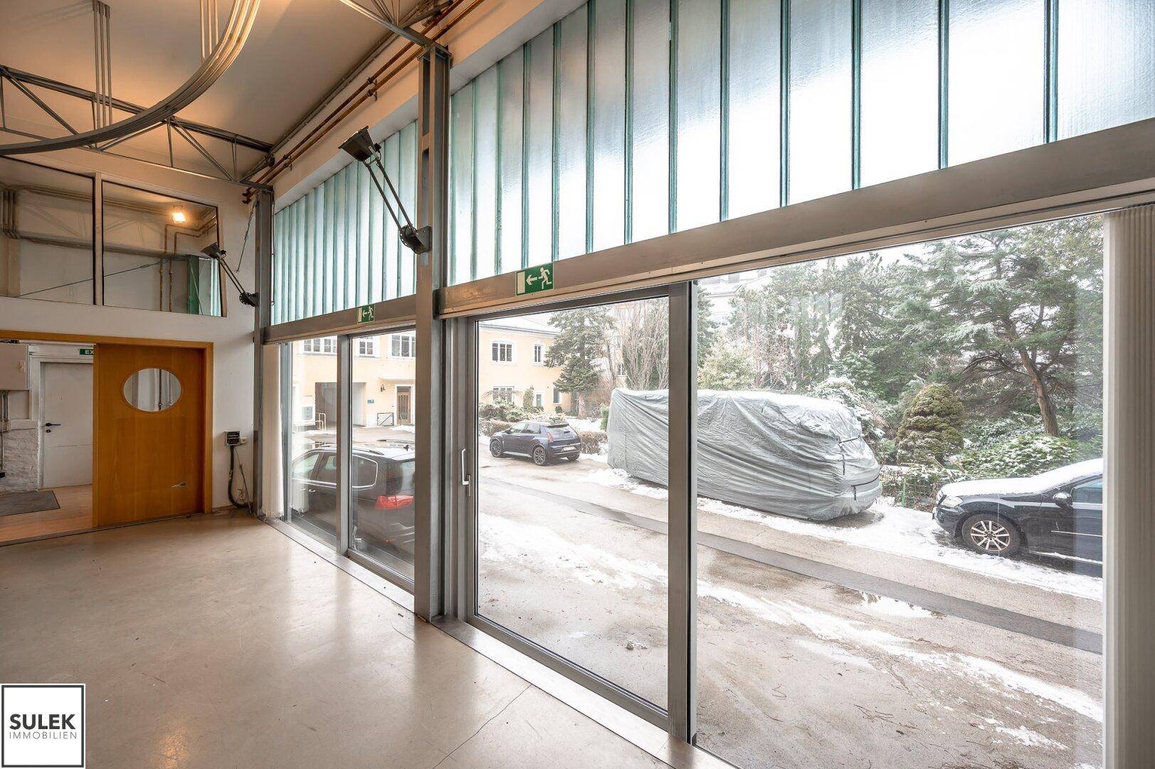 Große Glas-Schiebetüren im Eingangsbereich bieten Blick auf den verschneiten Außenbereich und geparkte Autos.