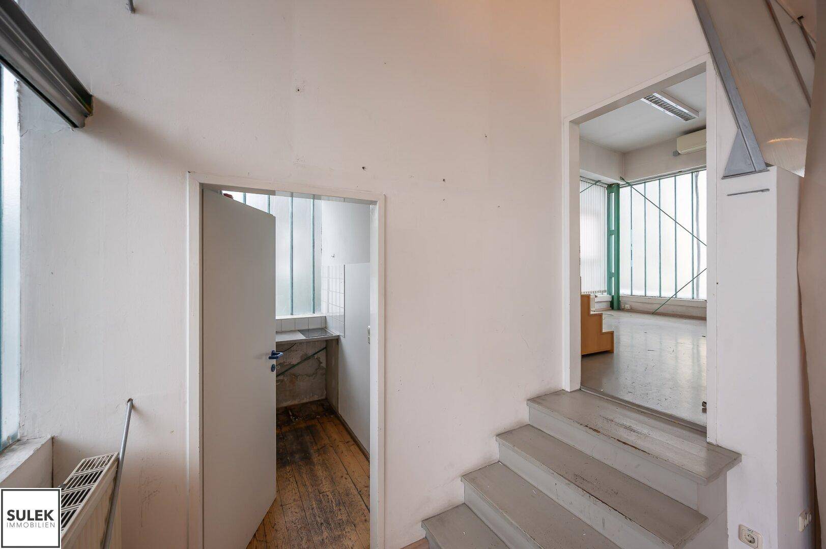 Flur mit Treppe und Zugang zu weiteren Räumen, darunter eine kleine Küche und ein Badezimmer.