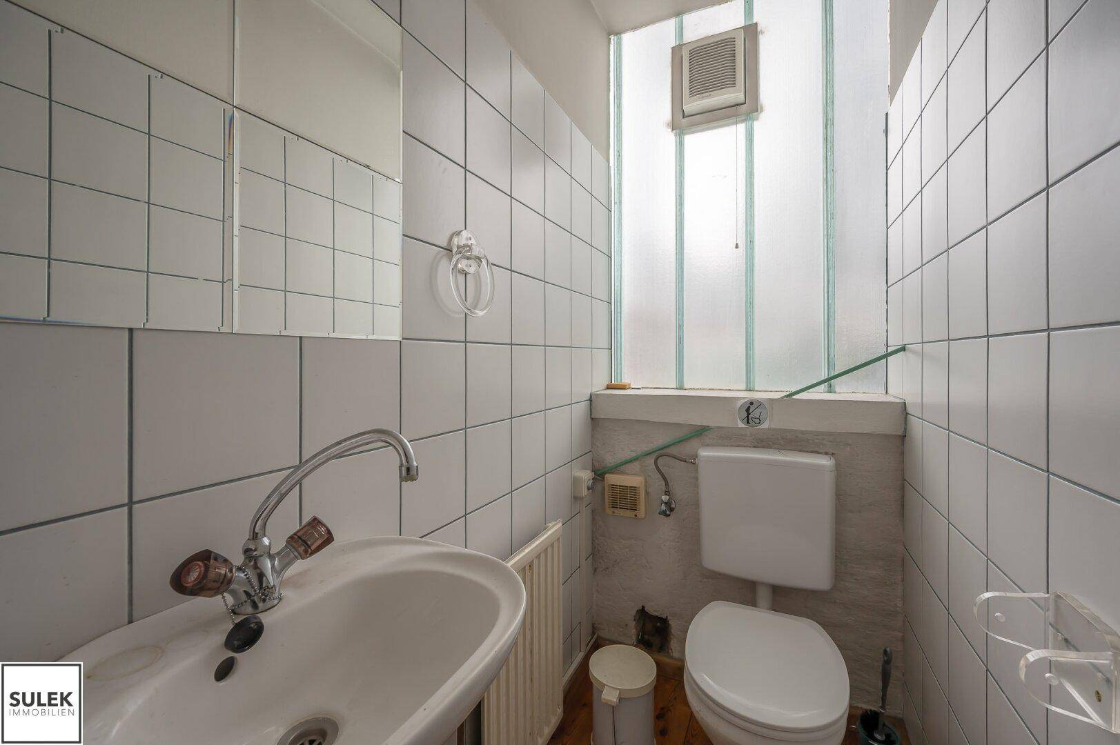 Kleines Badezimmer mit WC, Waschbecken und Fliesen an den Wänden, ausgestattet mit einem Fenster.