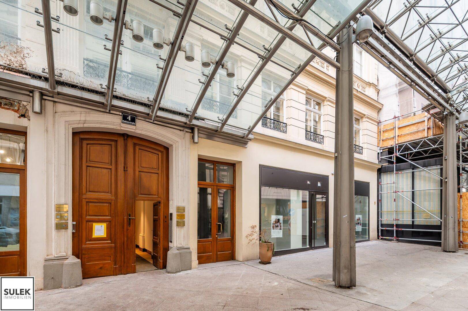 Historisches Gebäude mit imposantem Holztor und einer modernen Glasüberdachung über dem Eingangsbereich.