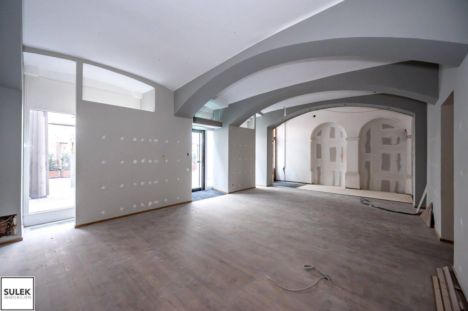 Weitläufiger Gewerberaum mit hohen, gewölbten Decken und vorbereiteten Wänden, ideal für flexible Gestaltungsmöglichkeiten.