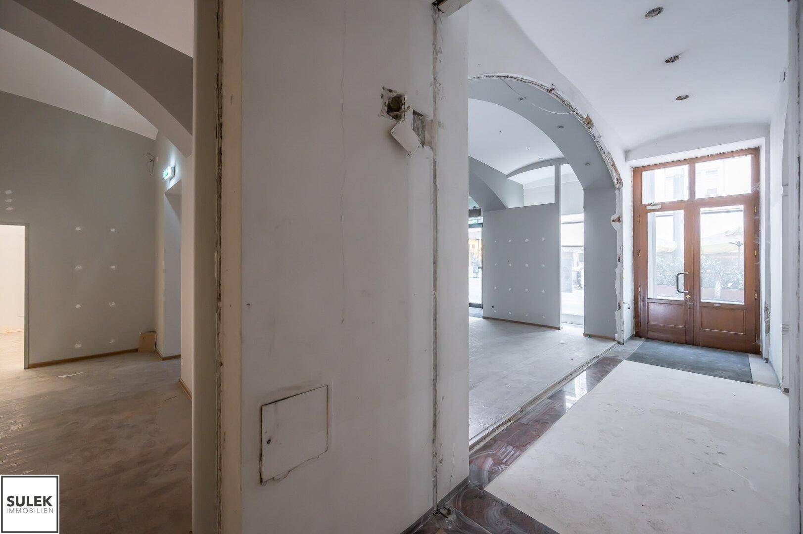 Eingangsbereich eines Gewerbeobjekts mit eleganten Holztüren und Marmorboden, der in den Hauptraum führt.