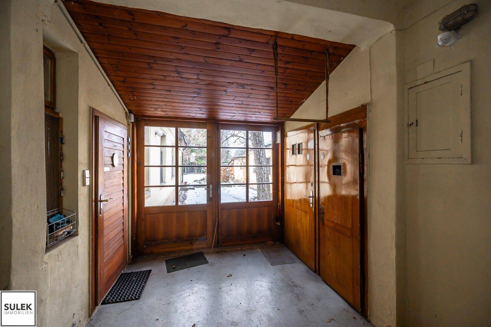 Überdachter Durchgangsbereich mit Holztäfelung an der Decke und Blick in den verschneiten Hof.