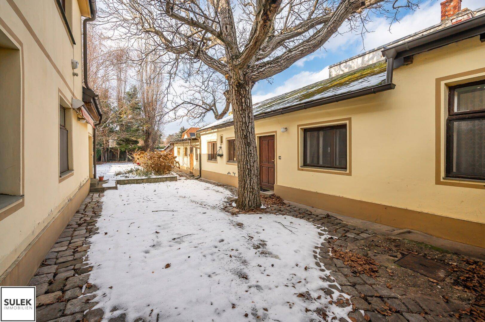 Verschneiter Innenhof mit altem Baum und Kopfsteinpflaster zwischen den Gebäudeteilen.