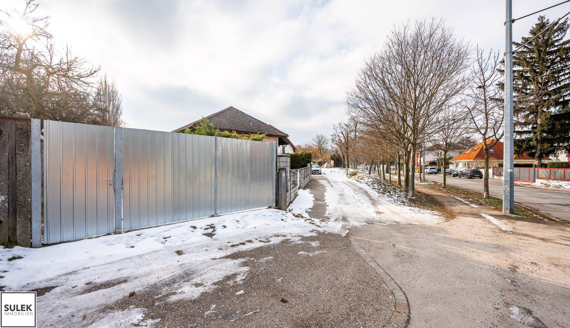 Zufahrt zum Grundstück mit großem Metalltor und verschneiter Straße im ländlichen Umfeld.