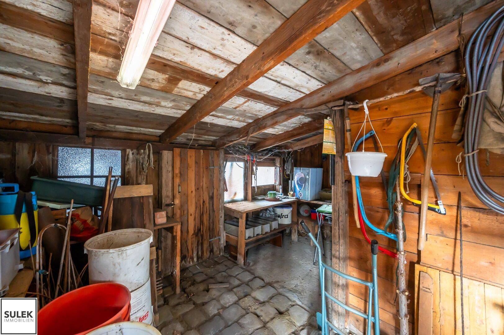 Rustikaler Werkstattraum mit Holzbalkendecke, Werkbank und verschiedenen Geräten und Materialien.