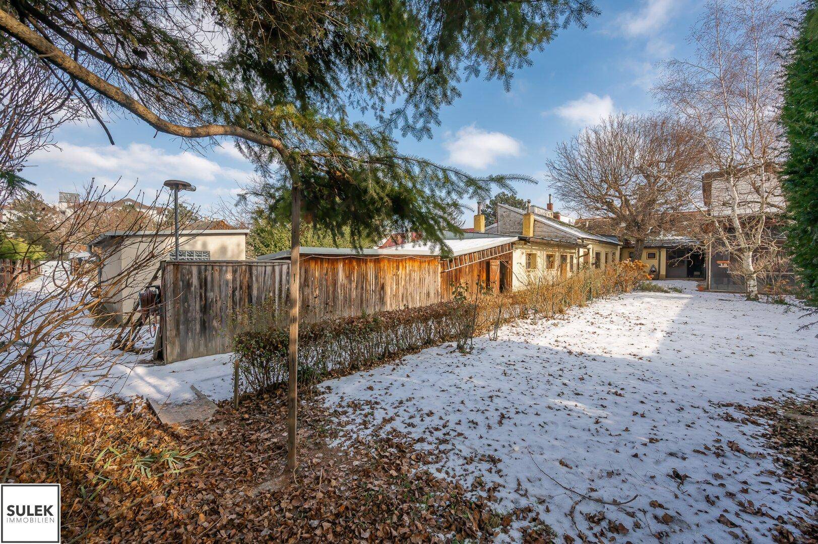 Weitläufiger Garten mit Schnee und Hecken, der zu den hinteren Gebäudeteilen führt.