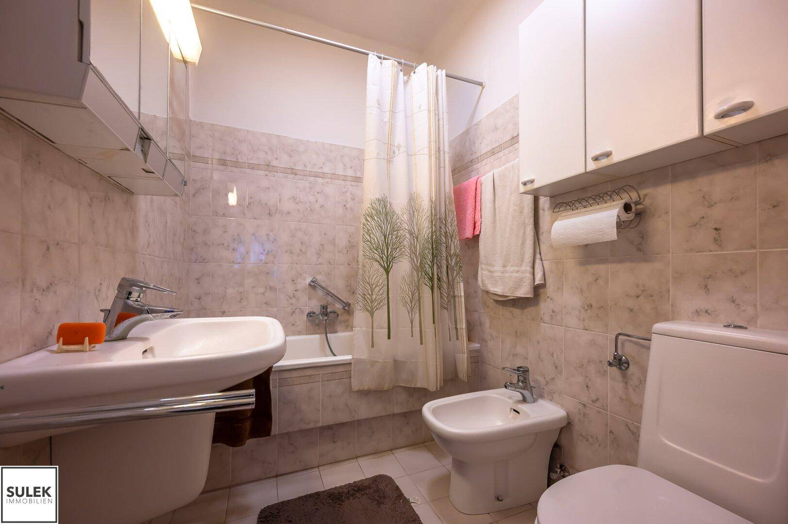 Badezimmer mit Badewanne, Bidet, WC und hellen Fliesen in einem älteren Stil.