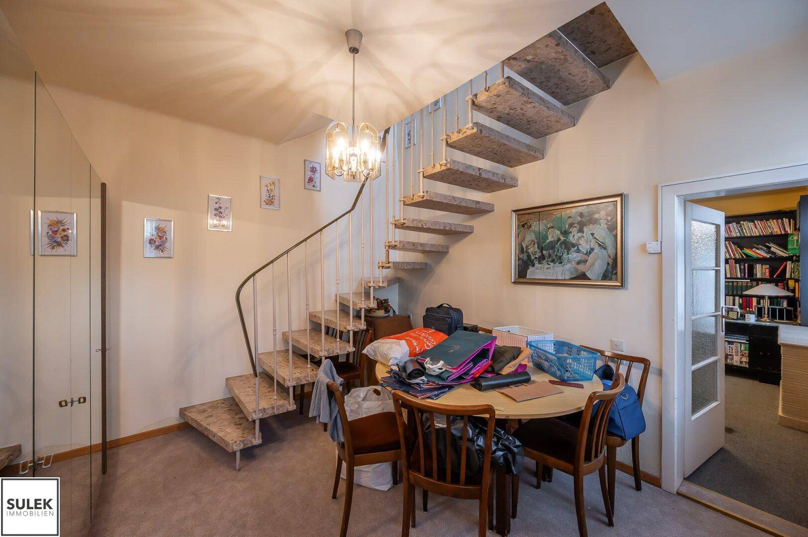 Wohnbereich mit Wendeltreppe, Esstisch und Blick auf einen Bücherregal im Hintergrund.