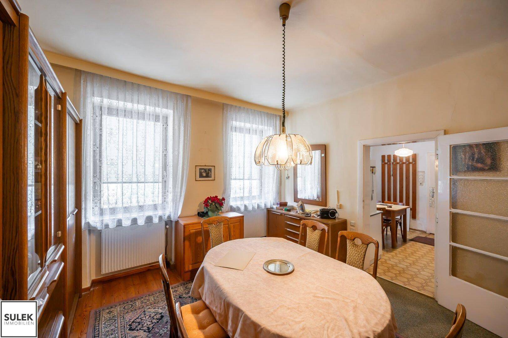 Esszimmer mit großem Fenster, Esstisch und Holzmöbeln, die eine gemütliche Atmosphäre schaffen.