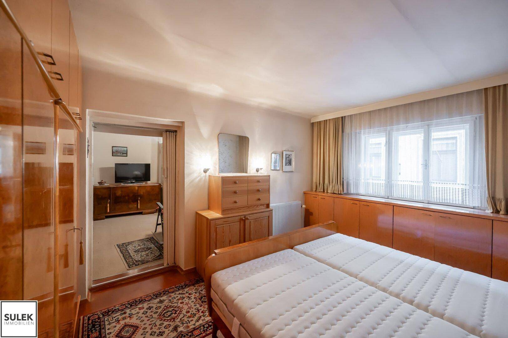 Schlafzimmer mit Doppelbett, Holzmöbeln und Zugang zu einem weiteren Raum.