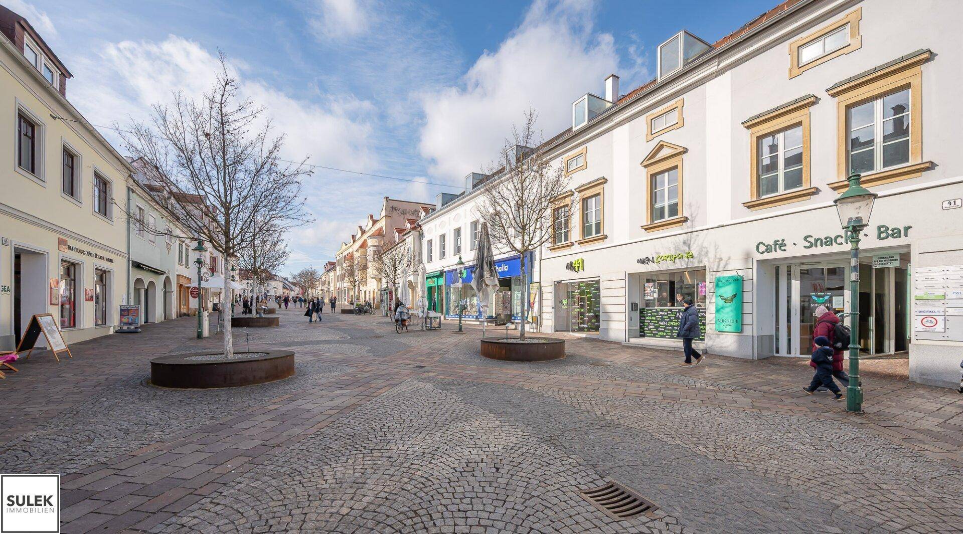 Belebte Einkaufsstraße mit Kopfsteinpflaster, Geschäften und Cafés.