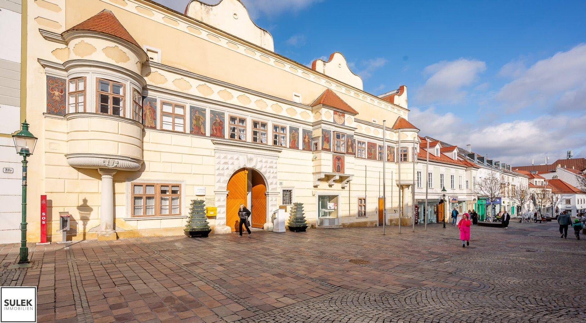 Historisches Gebäude mit kunstvollen Details an einem sonnigen Stadtplatz.