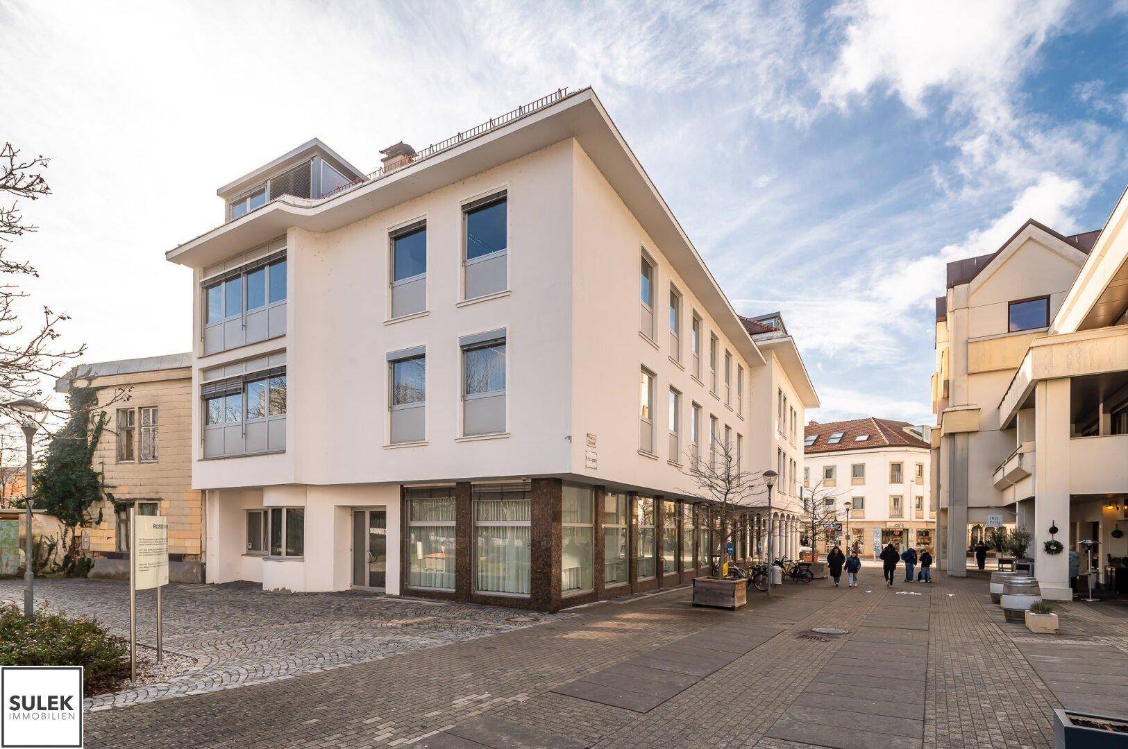 Modernes Geschäftsgebäude mit weißer Fassade und großen Fenstern in städtischer Umgebung.