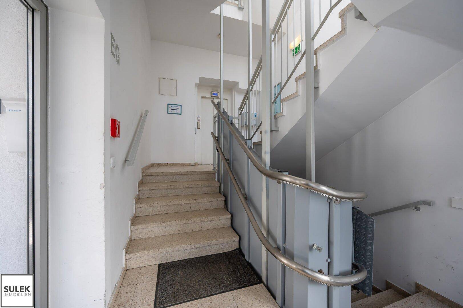 Treppenhaus mit Steinstufen und einem Rollstuhlrampenlift für Barrierefreiheit.