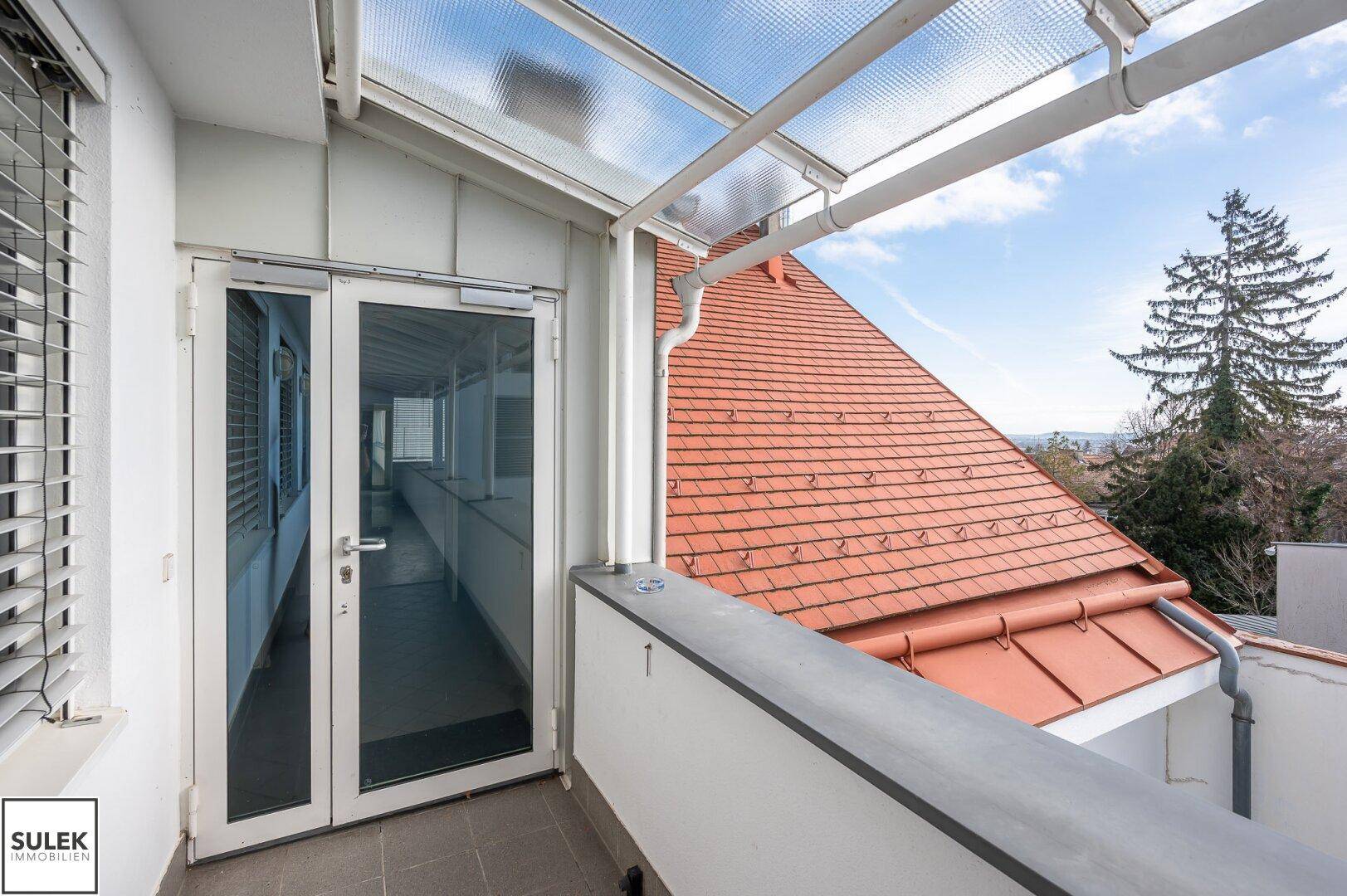 Überdachter Balkon mit Blick auf rote Ziegeldächer und die umliegende Landschaft.