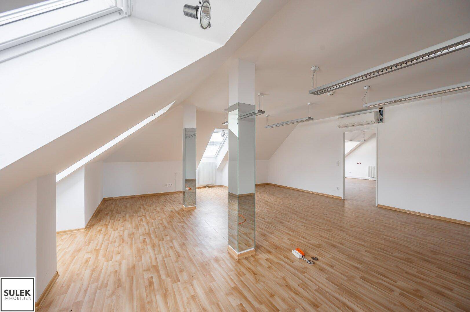 Geräumiger Büroraum mit Dachfenstern, Holzboden und modernen Deckenleuchten.