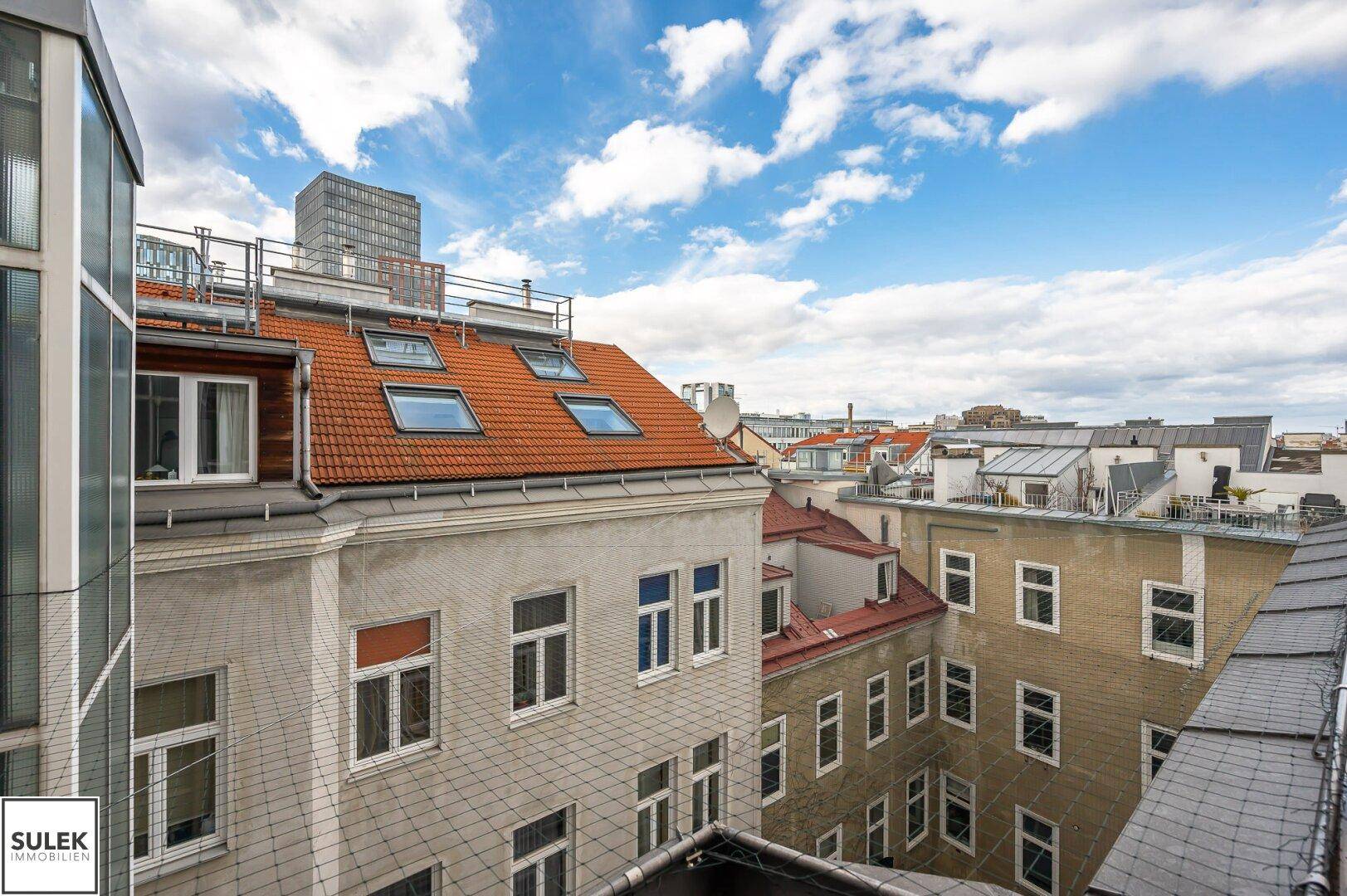 Blick über die Dächer der Stadt mit roten Ziegeln und blauem Himmel, umgeben von urbaner Architektur.