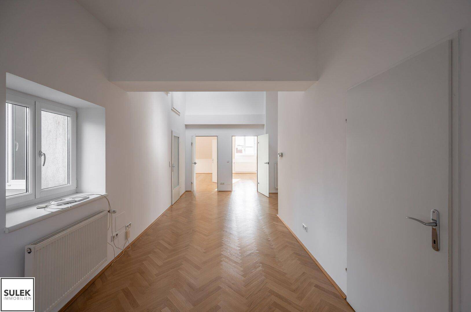 Langer, heller Flur mit Fischgrätparkett und einem Fenster, das den Eingangsbereich mit Licht versorgt.