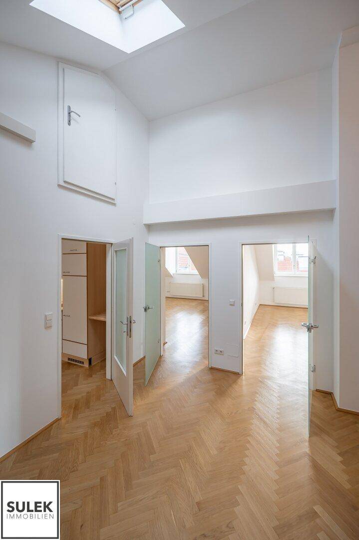 Heller Flur mit hohen Decken, Parkettboden und einem Dachfenster, das den Bereich erhellt.