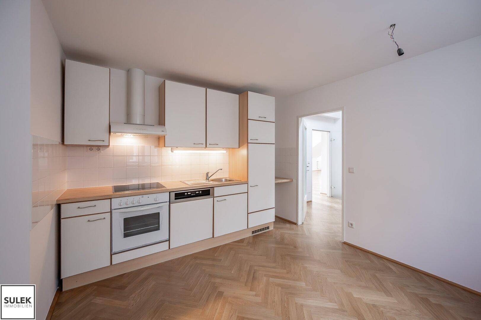 Funktionale Einbauküche mit weißen Schränken, Holz-Arbeitsplatte und integrierten Geräten.