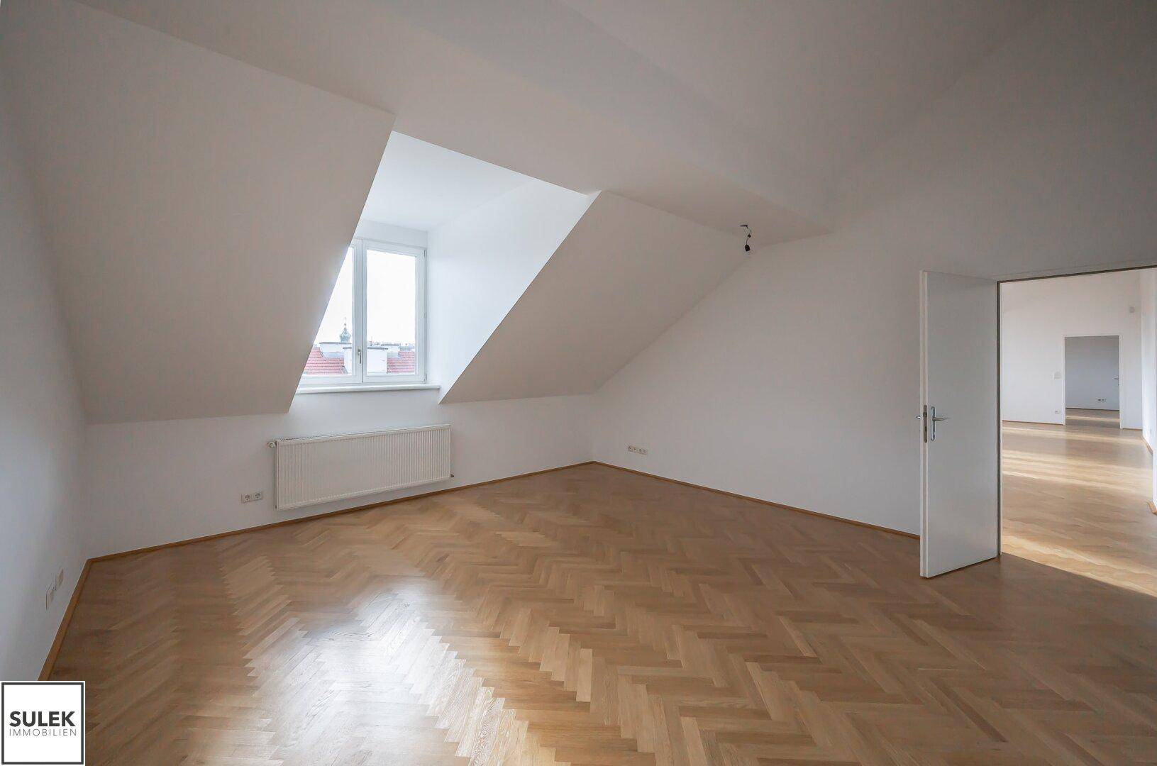 Geräumiges Zimmer im Dachgeschoss mit Fischgrätparkett und einem Fenster, das für natürliche Beleuchtung sorgt.
