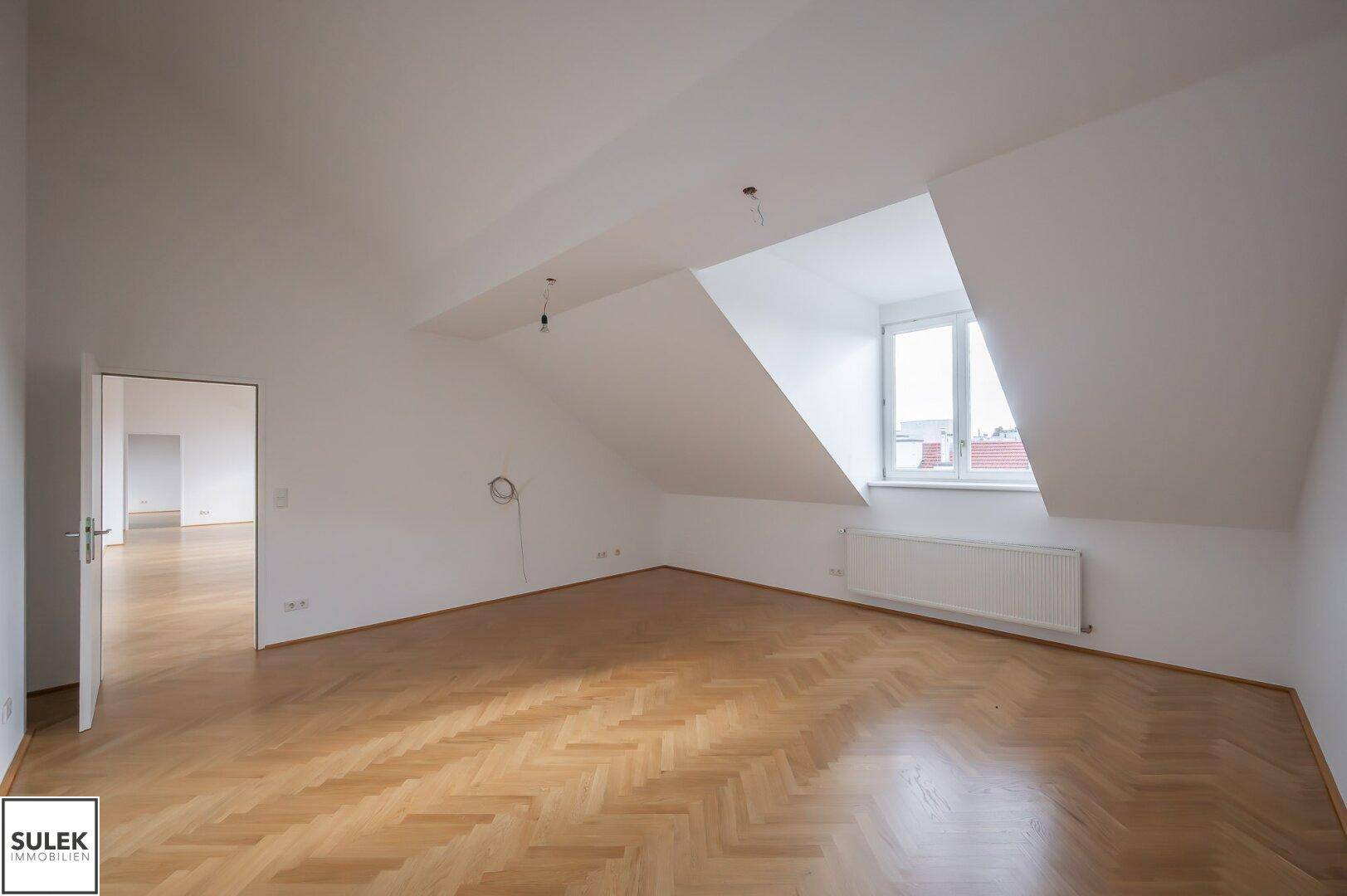 Helles Zimmer im Dachgeschoss mit Parkettboden und einem Fenster, das den Raum mit Tageslicht füllt.
