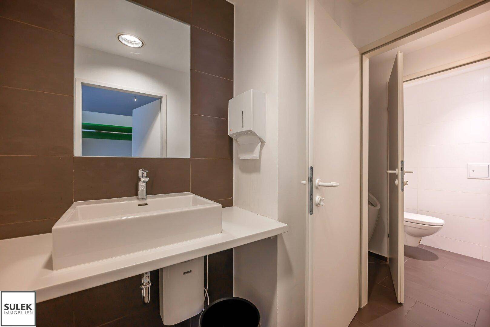 Modernes Badezimmer mit Aufsatzwaschbecken, großem Spiegel und braunen Wandfliesen.
