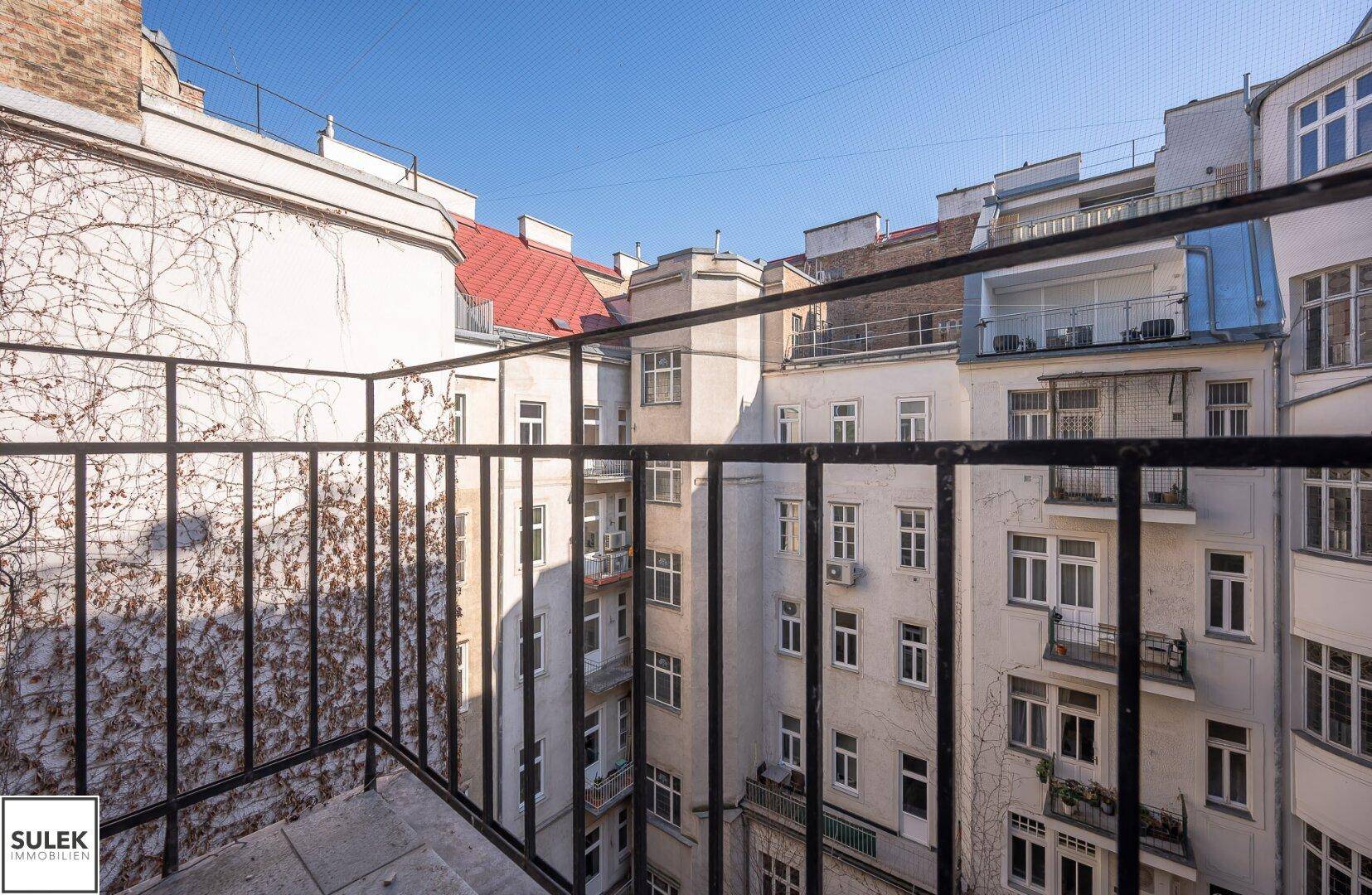 Kleiner Balkon mit Metallgeländer und Blick auf den Innenhof eines Altbaus.