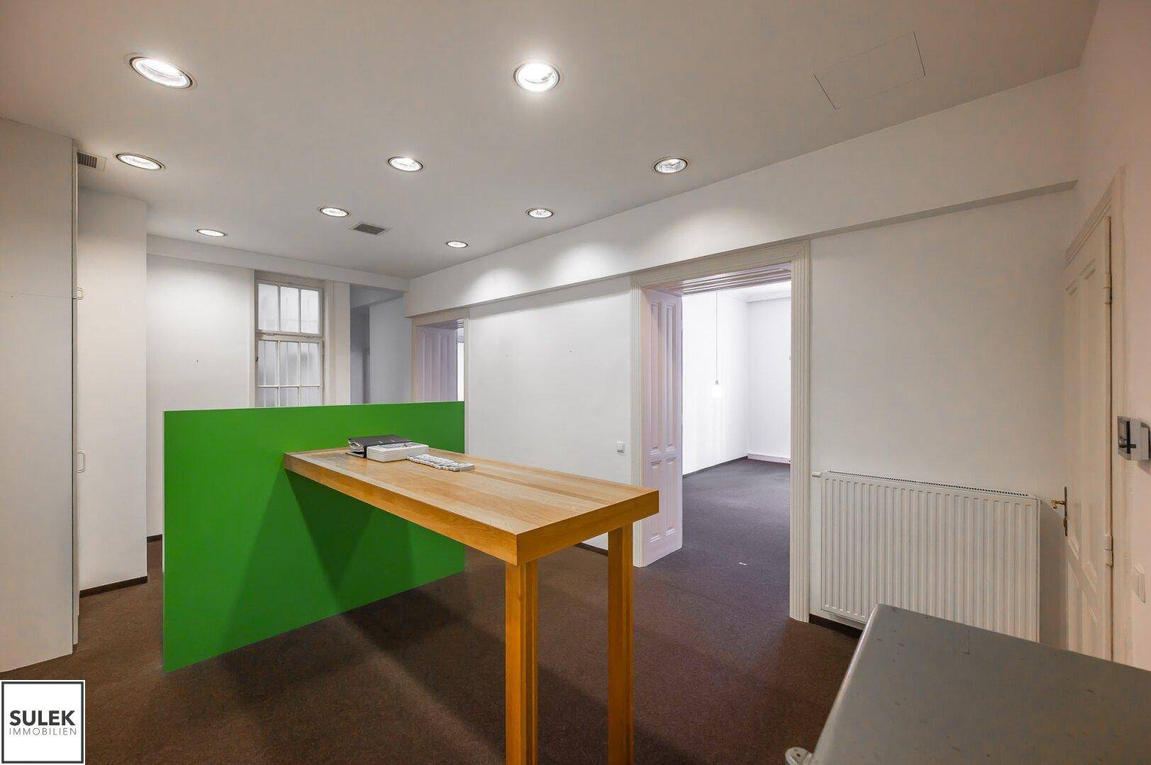 Moderner Bürobereich mit Einbaustrahlern, einem grünen Raumteiler und Holztisch.
