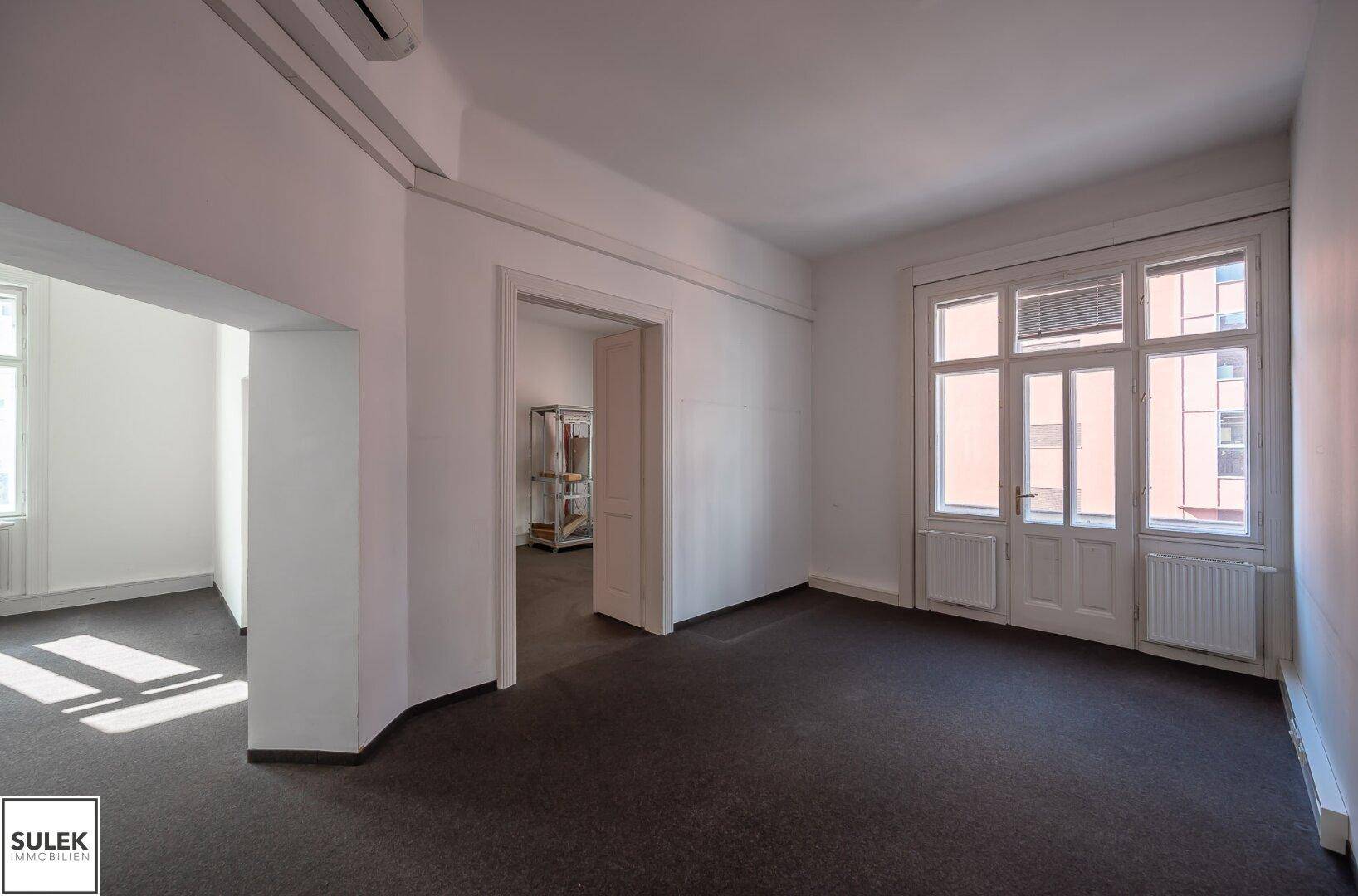 Büroraum mit Teppichboden, Klimaanlage und einer Tür, die zu einem Balkon führt.