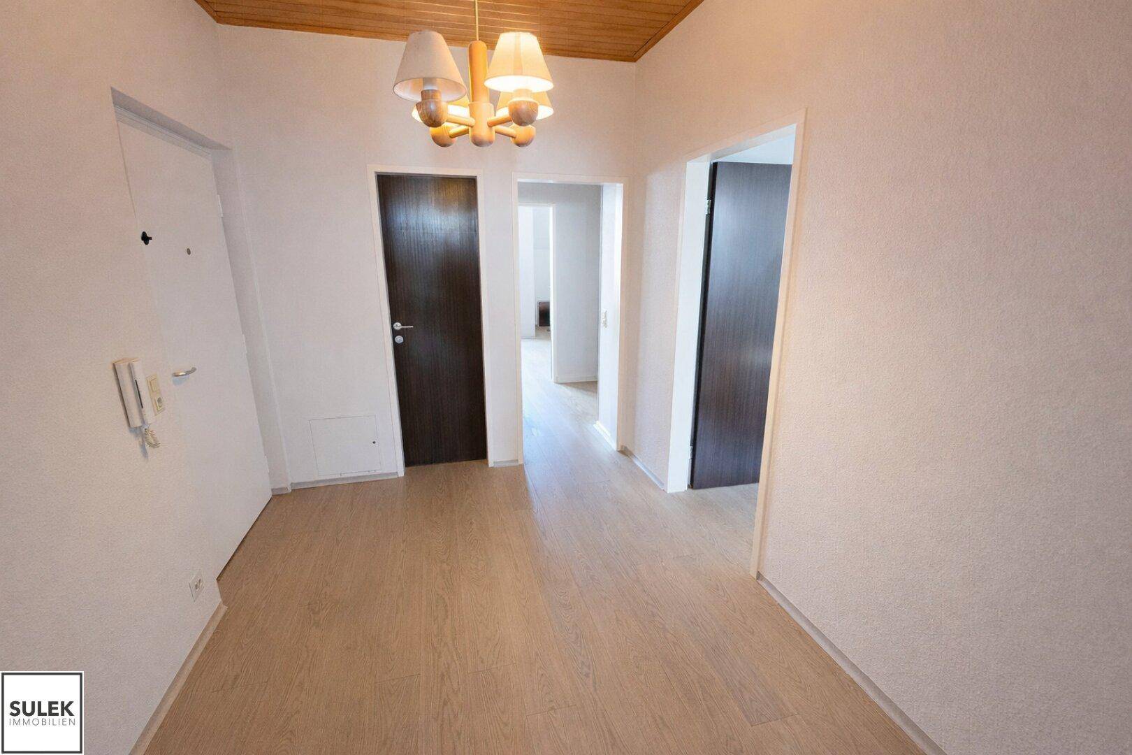 Heller Eingangsbereich mit Holzdecke und Laminatboden, der zu weiteren Räumen führt.