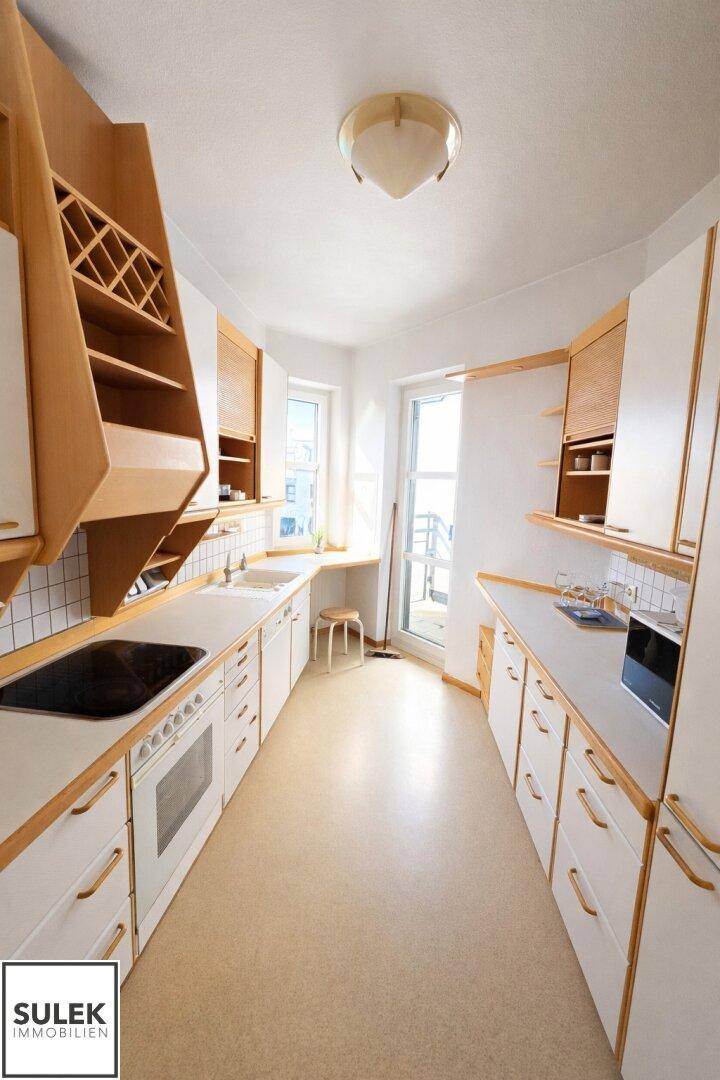 Funktionale Küche mit hellen Holzschränken, Einbaugeräten und Fenster mit Ausblick.