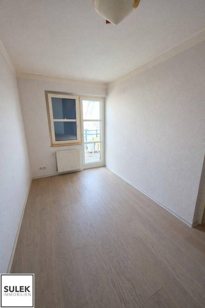 Helles Zimmer mit Laminatboden und Fenster, das Zugang zu einem Außenbereich bietet.