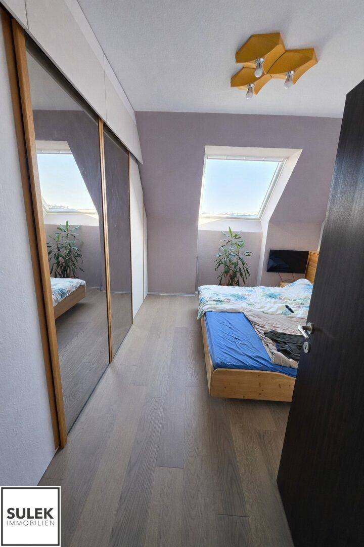 Schlafzimmer mit Laminatboden, Dachfenster und praktischen Einbauschränken entlang der Wand.