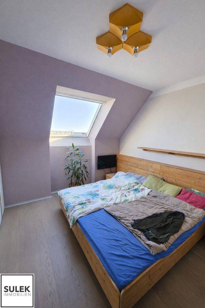 Gemütliches Schlafzimmer im Dachgeschoss mit Holzbett, Laminatboden und Dachfenster.