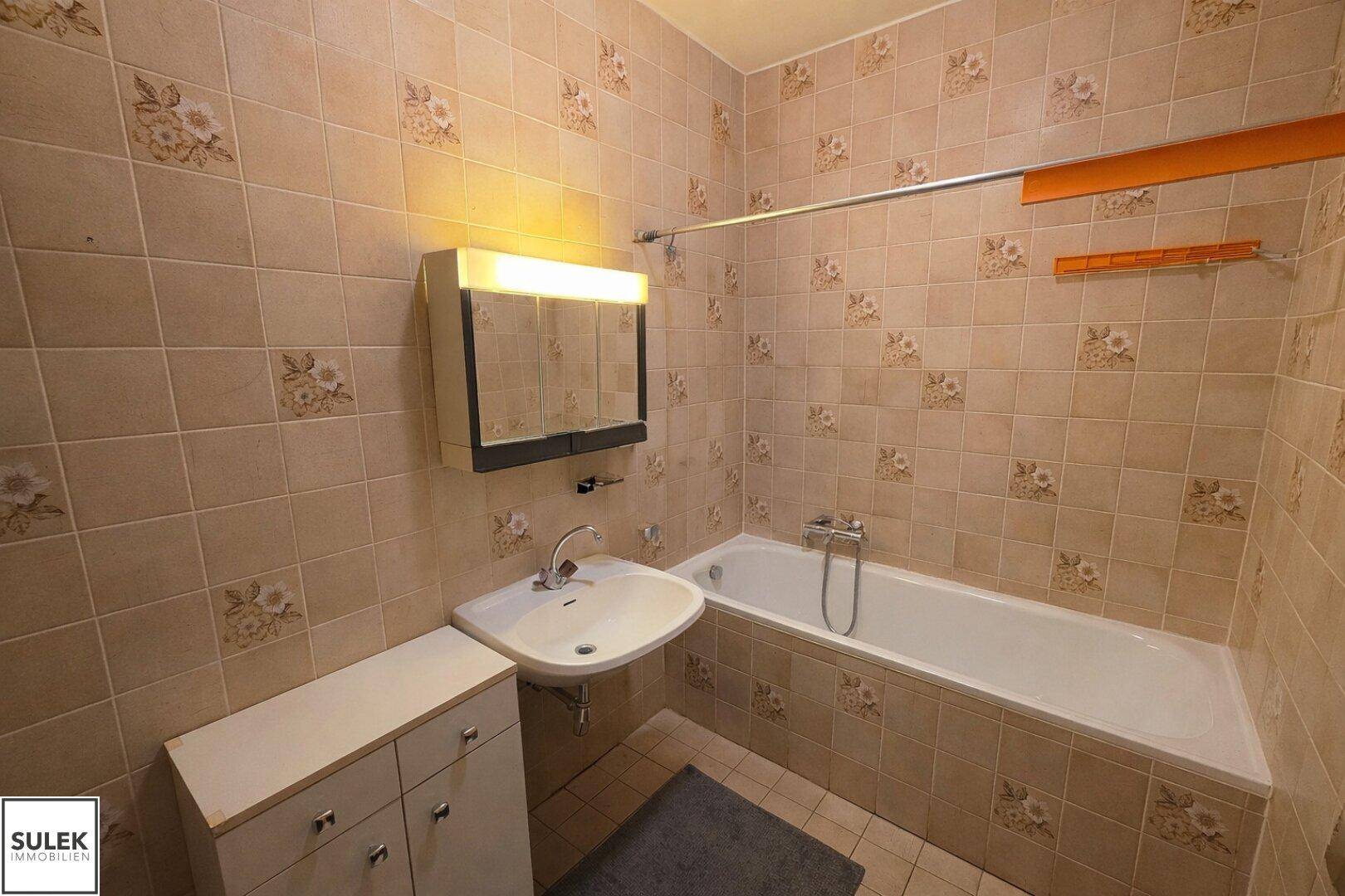 Badezimmer mit Badewanne, Waschbecken und gemusterten Fliesen im Retro-Stil.