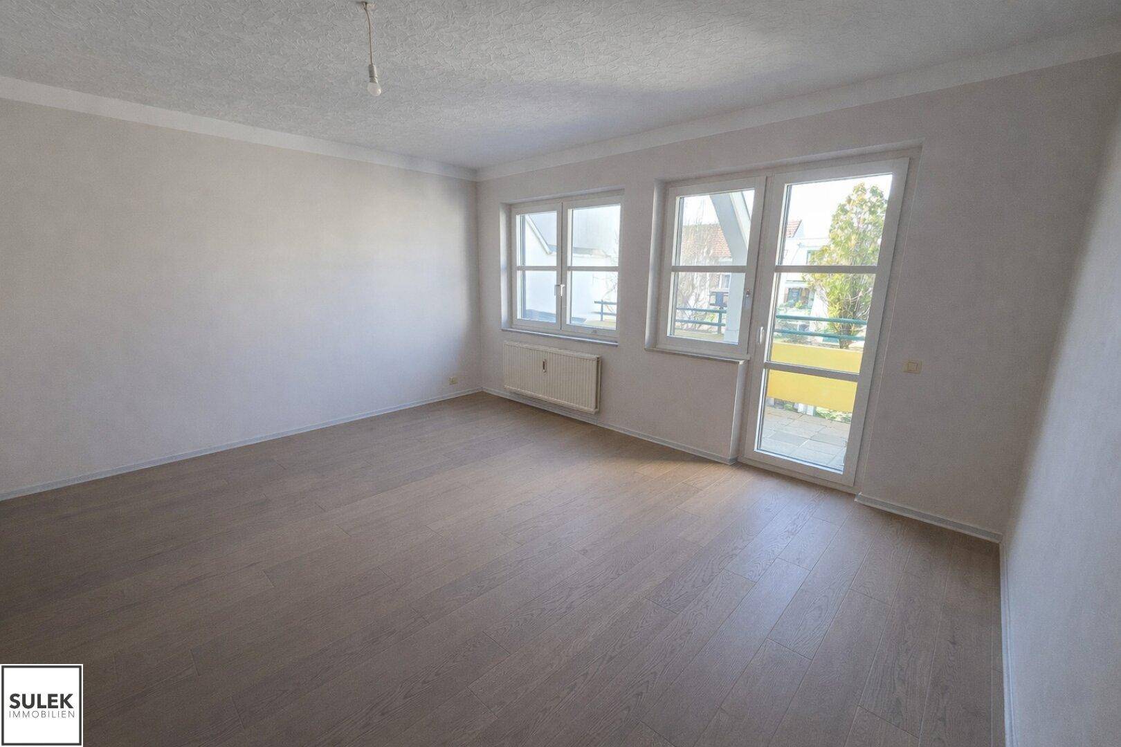 Geräumiges Wohnzimmer mit Laminatboden, großen Fenstern und direktem Zugang zum Balkon.